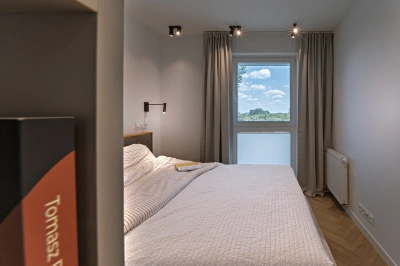 Projekt minimalistycznego wnętrza na Mokotowie w stylistyce nawiązującej do lat 60tych &ndash; wąski regal na książki na zewnętrznej krawędzi szafy ubraniowej w sypialni