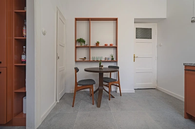Projekt kuchni w modernistycznej willi pod Warszawą - za okrągłym stołem jadalnianym umieściłyśmy p&oacute;łkę na dekoracyjne i funkcjonalne drobiazgi w kolorze terakoty.