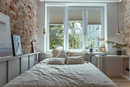 Projekt sypialni w kamienicy na Mokotowie. Duże dwuosobowe łóżko posiada wezgłowie o wysokości dopasowanej do parapetu.